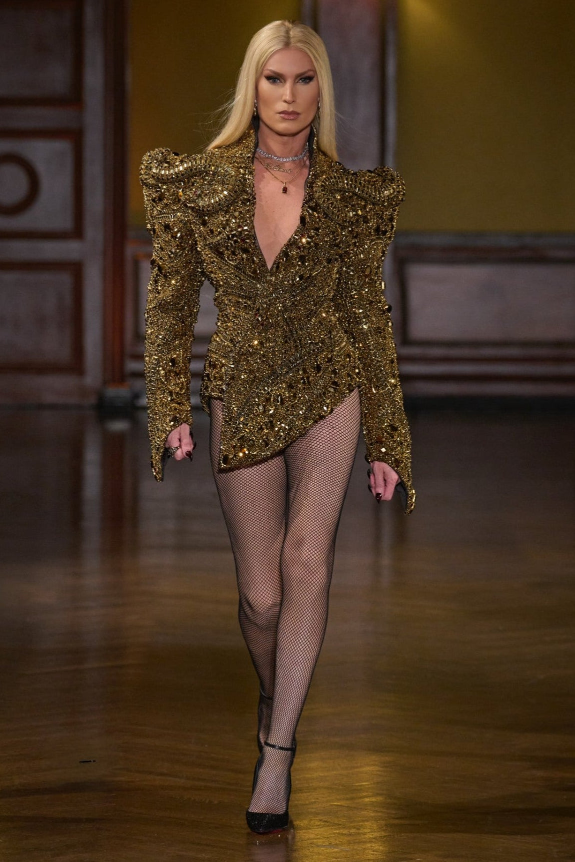 PHILLIPPE BLOND walking on a runway in a gold sequin dress with a dark background